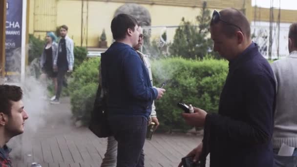 SAN PETERSBURG, RUSIA - 28 DE MAYO DE 2016: La compañía de hombres fuma cigarrillos electrónicos sentados en el banco, hablando. Evento de pañales — Vídeos de Stock