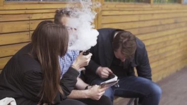 Saint Petersburg, Rusya - 28 Mayıs 2016: Genç kız ve erkekler bankta elektronik sigara içiyorum. Vapers. Alt kültür