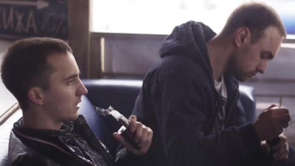 Twee vapers rook elektronische sigaret zittend op fauteuil. Rokers. Stoom. — Stockvideo