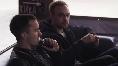 Genç erkek koltukta oturan elektronik sigara. Vapers. Buhar çok