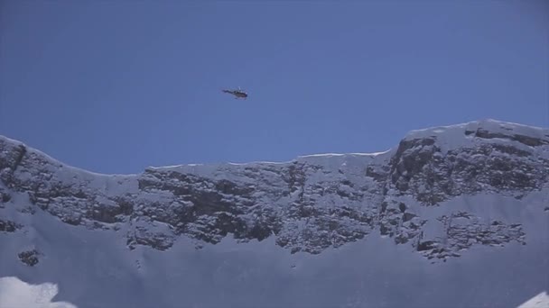 Helicopter fly above snowy peaks of mountains. Blue sky. Sunny day. — Stock Video
