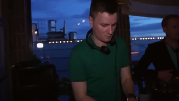 DJ przędzenia na gramofon na party w klubie nocnym. Człowiek z saksofon. Słuchawki. — Wideo stockowe