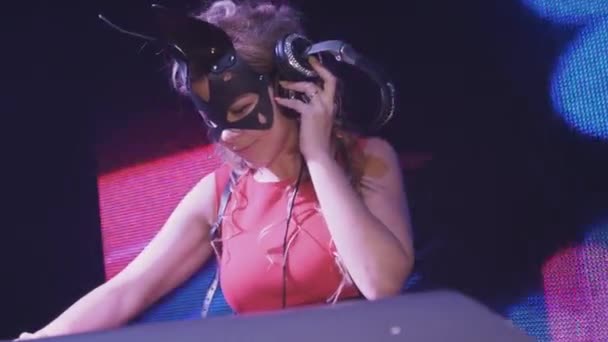 Gadis DJ bertopeng kelinci, gaun merah berputar di meja putar di klub malam. Headphone . — Stok Video