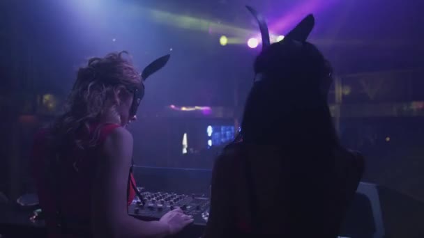 Back side mc girl and Dj girl in hare masks spinning at turntable in nightclub. — Stock Video