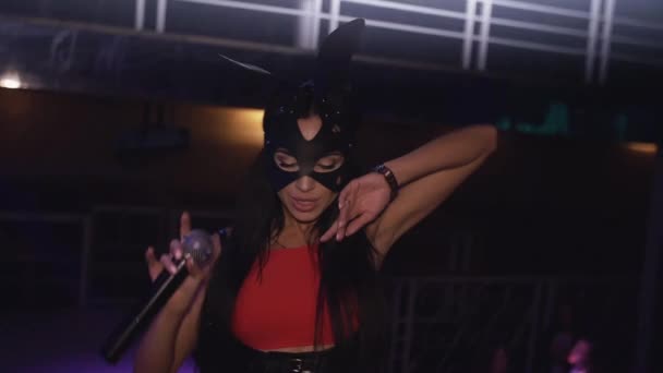 Morena chica mc en traje de cuerpo rojo máscara liebre en el escenario en discoteca. Mira en la cámara — Vídeos de Stock