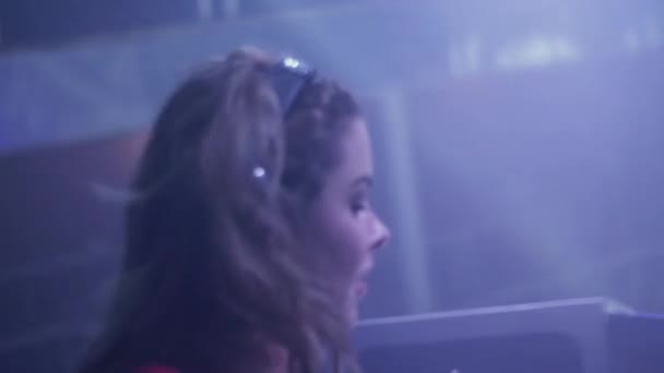 DJ-Mädchen mit Kopfhörern dreht sich und tanzt am Plattenteller in einem Nachtclub. Blitzlichtgewitter. — Stockvideo