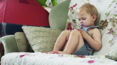 Sarışın küçük çocuk kanepe daire dokunun smartphone içinde oturmak. Aygıt. Çocukluk