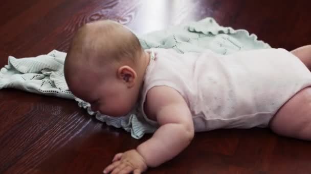 Um bebé adorável deita-se no chão com o estômago. Apartamento. Chorando. Movimentos . — Vídeo de Stock