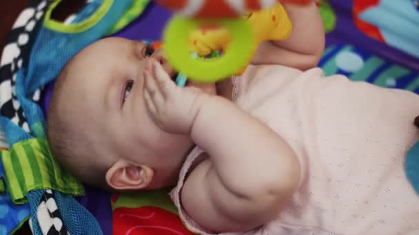小さな赤ちゃんは、口の中で保持しているベビーベッド、おもちゃで遊んでにあります。母性. — ストック動画