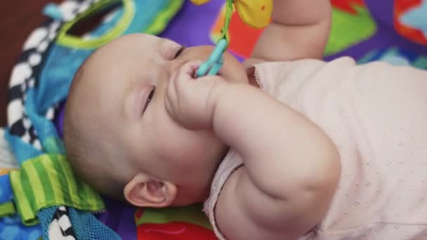 Noworodek leży łóżeczku niemowlęcym bawi się zabawkami, trzymając w ustach. Ładna. Macierzyństwo. — Wideo stockowe