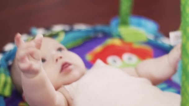 Ein entzückendes kleines Baby liegt auf einem Teppich und spielt mit aufgehängten Spielzeugen. Niedlich. Mutterschaft — Stockvideo