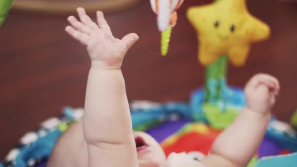 Adorable bebé se acuesta en la alfombra tocando los juguetes por las manos. Lindo. Maternidad. Niño. — Vídeo de stock