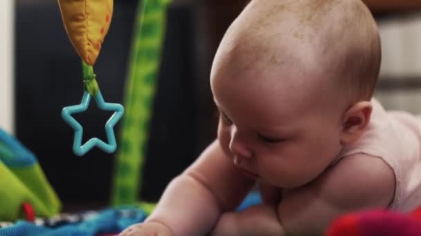 Adorable bebé jugando con el juguete en la alfombra de los niños en desarrollo. Mira en la cámara — Vídeos de Stock