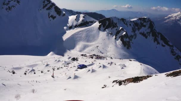 Blick auf Skigebiet in schneebedeckten Bergen bei sonnigem Tag. Skifahrer und Snowboarder. Pisten. Sprungbrett — Stockvideo