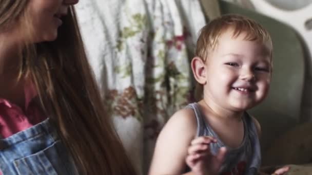 La jeune mère a mis la chaussette sur la jambe du fils. La maternité. Boy vague main dans la caméra 