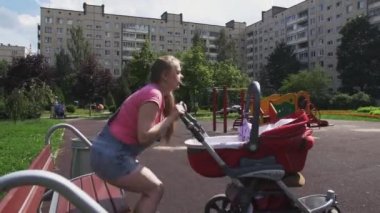 Genç anne Bahçesi bankta oturmak. Kırmızı bebek arabası. Annelik. Güneşli