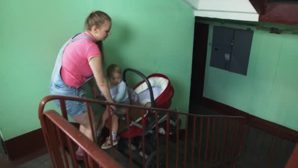 年轻的母亲走出公寓从楼梯放下童车。家庭. — 图库视频影像