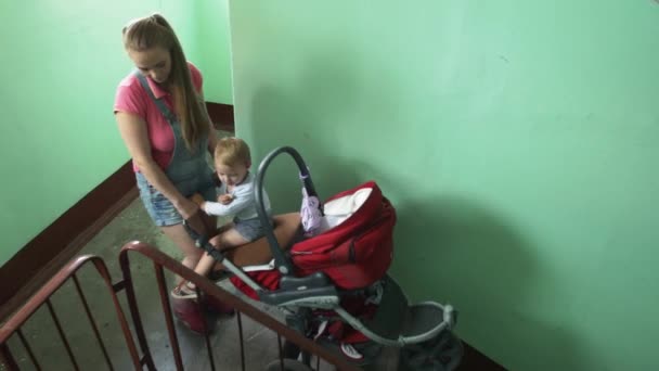 La jeune mère a posé un landau rouge dans les escaliers. La maternité. Petit garçon. . — Video