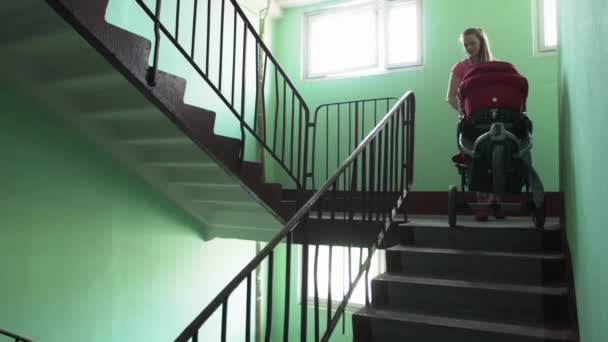 Young mother put down red baby carriage from stairs. Motherhood. Little son. — Stock Video