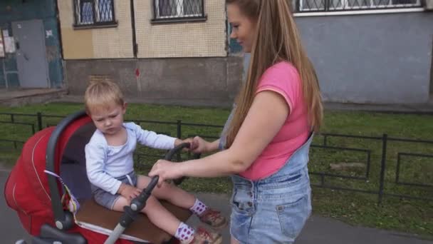 Mladá matka chůze s kočárkem. Mateřství. Malý syn sedět na vozíku — Stock video