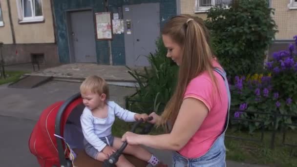 Junge Mutter zu Fuß mit Kinderwagen. Familie. Kleiner Sohn sitzt auf Kutsche — Stockvideo