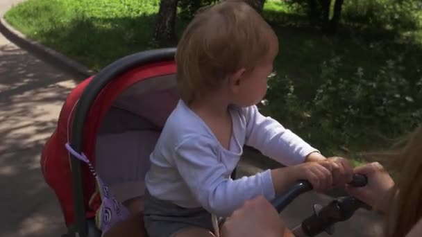 Mamma rida barnvagn. Moderskap. Lille son sitter på vagnen. Solig dag — Stockvideo