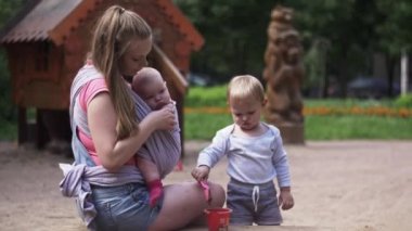 Genç anne tut bebek askı içinde oyun sanal oğluyla. Bahçesi. Aile
