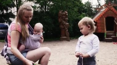 Genç anne tut bebek sapan oyunda oğlu ile sahada. Kum. Yaz