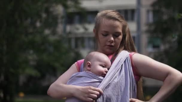 Giovane madre legare fionda bambino tenendo bambino piccolo. La maternità. Giornata estiva . — Video Stock