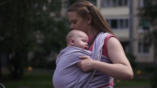 Madre joven sostiene al niño con cabestrillo de bebé. Caminando por la calle. Día de verano. Maternidad — Vídeos de Stock