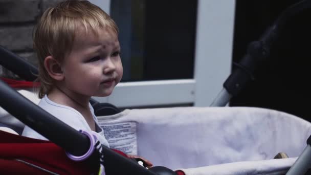 Il bambino biondo gioca con il giocattolo in carrozza per strada. Giornata estiva. Bambino. — Video Stock