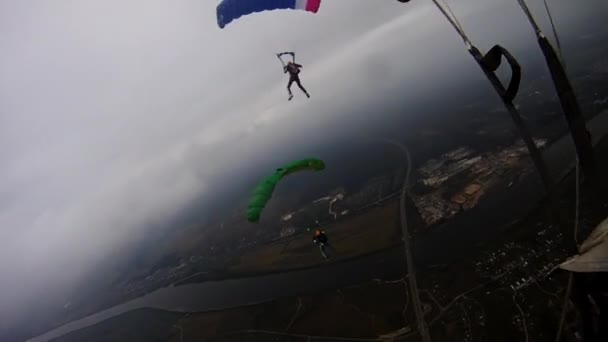 Fallskärmshoppare med färgglada fallskärmar flyga över gröna fält i molnig himmel. Extreme — Stockvideo