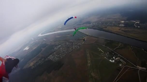 Skydivers με πολύχρωμα αλεξίπτωτα ισορροπία στον ουρανό πάνω από το πράσινο πεδίο. Tandem. — Αρχείο Βίντεο