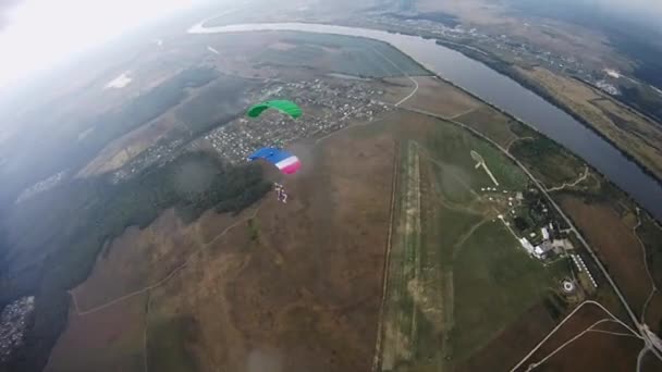 Paracaidistas con paracaídas de colores equilibran en el cielo sobre el campo verde. Río . — Vídeos de Stock