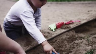 Genç anne bekle bebek sapan oyunda oğlu ile kum Bahçesi. Yaz günü