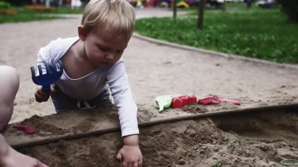 Молодая мать держит милый ребенок в стропе играть с сыном на детской площадке. Саммер. Песок — стоковое видео