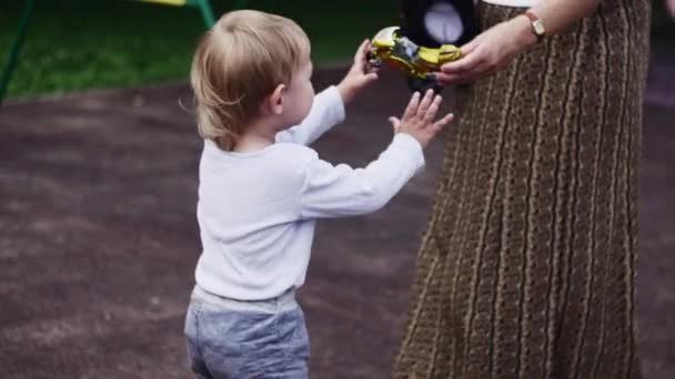 Vrouw teruggeven motor speelgoed huilende jongen op speelplaats. Zonnige dag. Jeugd — Stockvideo