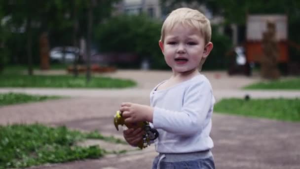 Маленький хлопчик на ігровому майданчику з мотоциклетною іграшкою. Сонячний день. Дитинство. Літо — стокове відео