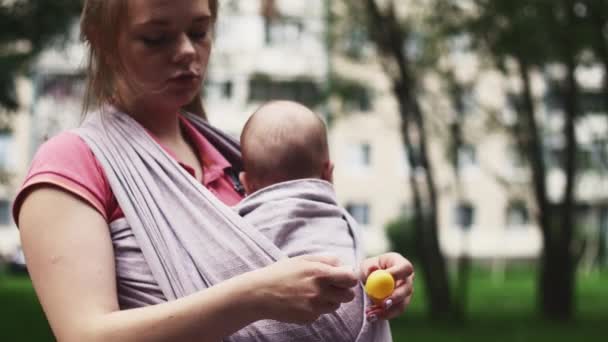 Μητέρα με μωρό στο sling, αγόρι φαγητό kinder έκπληξη για μεταφορά του μωρού. Η μητρότητα — Αρχείο Βίντεο