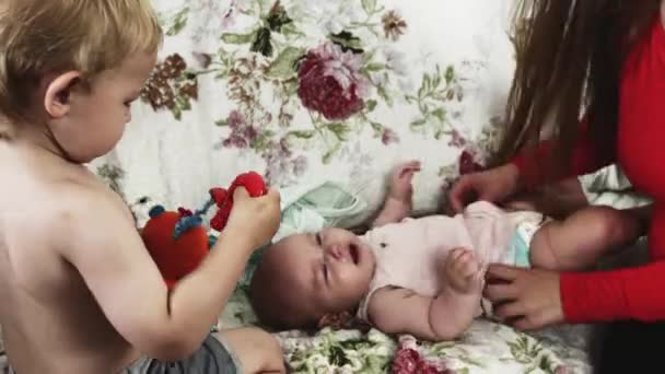 Jonge moeder aankleden huilen baby op sofa met zoontje. Moederschap. Zorg — Stockvideo