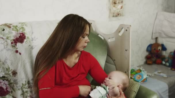 Jonge moeder in rood shirt borstvoeding beetje huilende baby op Bank. Moederschap. — Stockvideo