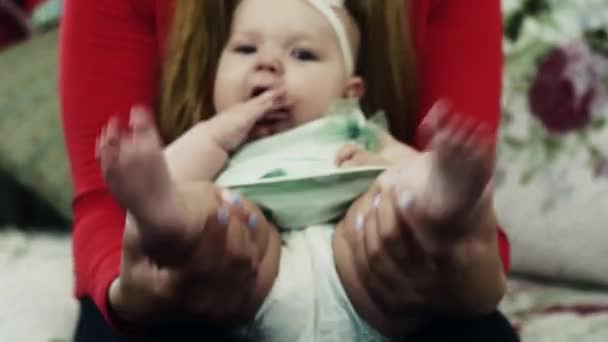 Fiatal anya, piros póló imádnivaló baba játszani a kanapé. Anyaság. szerelem — Stock videók