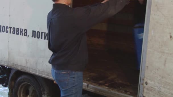 Volwassen sterke man neemt grote blauwe container met grepen uit het leveren van auto van op straat. Levering — Stockvideo