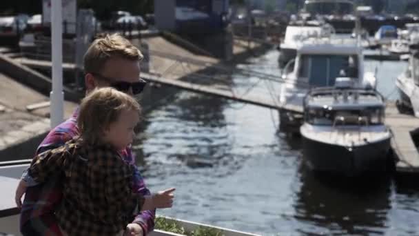 Far håller lille son på händer promenader vid havet. Händelse. Solig sommardag. — Stockvideo