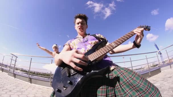 Man in skirt play electric guitar on seafront in sunny day. Girl dance in ballerina suit. Rock — Stock Video