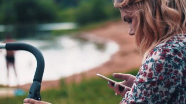 Anne Bebek arabası ve gölde smartphone kullanarak sway. Yaz günü. Yürüyüş