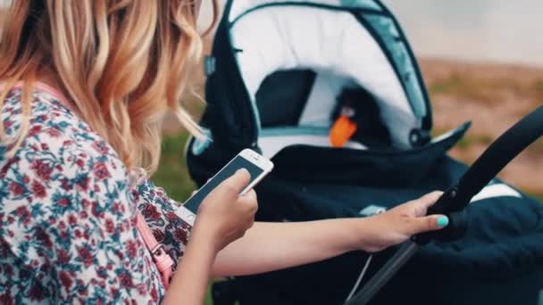 Мати катається на дитячих колясках і використовує смартфон у парку. Літній сонячний день . — стокове відео