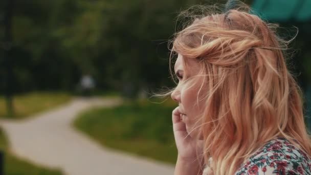 Mor sitter på bänken och tala på telefon i park. Vajande barnvagn. — Stockvideo