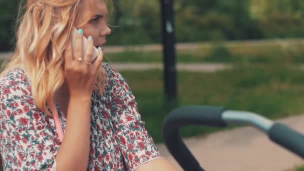 어머니는 유모차와 말하기 공원에 전화에 흔들리고 있습니다. 여름 날입니다. 임산부 — 비디오