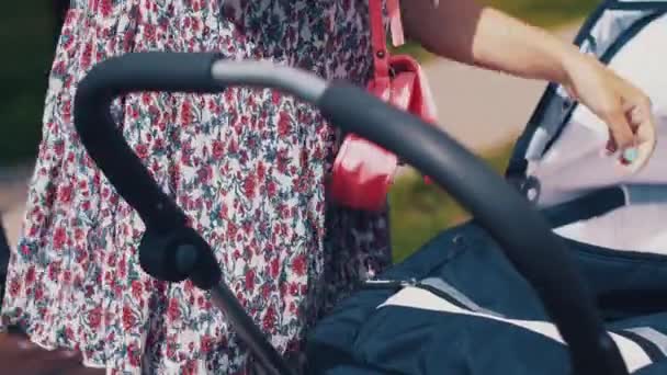 Moeder zwaaien kinderwagen en spreken op telefoon op straat. Zomerdag. Mothercare — Stockvideo